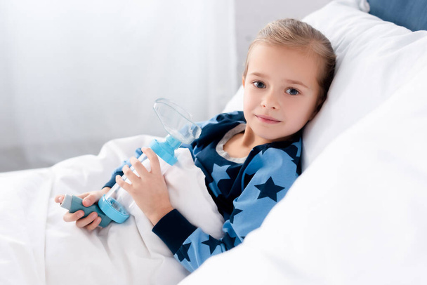 喘息の子供保持吸入器とともにベッドルームに横たわっている間 - 写真・画像