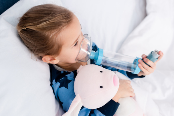 sick kid using inhaler with spacer and holding soft toy - Photo, Image