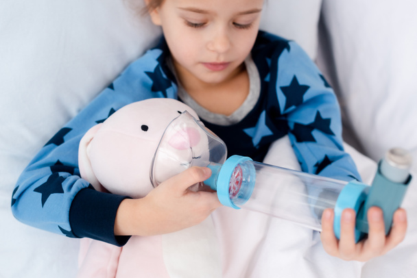 επιλεκτική εστίαση του άρρωστου παιδιού κρατώντας εισπνευστήρα με αποστάτη κοντά παιχνίδι λαγουδάκι  - Φωτογραφία, εικόνα