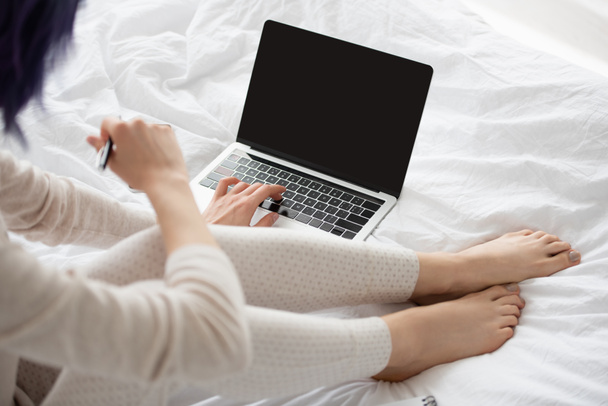 Vista recortada do freelancer com caneta trabalhando no laptop na cama
 - Foto, Imagem
