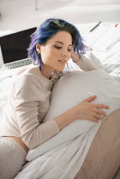 Freelance rêveuse avec des cheveux colorés couché près d'un ordinateur portable sur le lit
  - Photo, image
