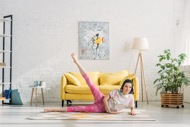 Girl with colorful hair stretching and looking away on floor in living room - Foto, afbeelding