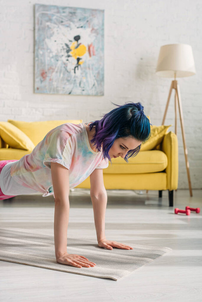 Koncentrált nő színes hajjal csinál deszka jóga szőnyeg a nappaliban - Fotó, kép