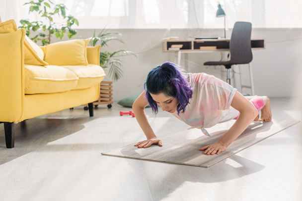 Fille avec des cheveux colorés faisant push-ups sur tapis de fitness dans le salon
 - Photo, image