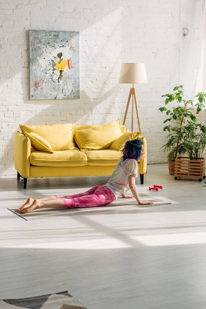 Girl with colorful hair in cobra pose on yoga mat in living room - Foto, Imagem