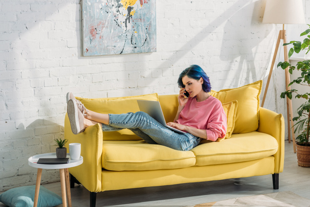 Freelance avec des cheveux colorés parler sur smartphone avec ordinateur portable et couché sur le canapé
 - Photo, image