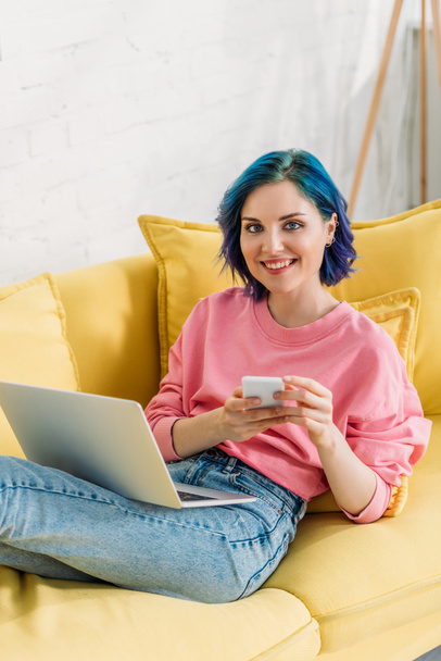 Libero professionista con capelli colorati, smartphone e laptop sorridente e sdraiato sul divano
 - Foto, immagini
