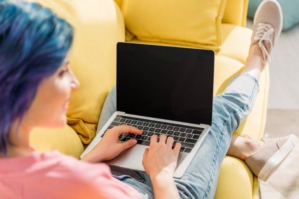 Enfoque selectivo del freelancer con cabello colorido y portátil sonriendo y acostado en el sofá
 - Foto, imagen