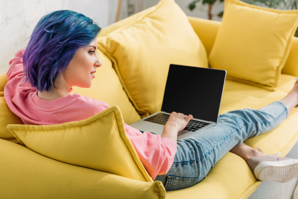 Freelancer con el pelo colorido y portátil sonriendo y acostado en el sofá en la sala de estar
 - Foto, imagen