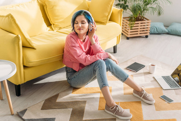 High angle view of freelancer with colorful hair, closed eyes and headphones smiling near sofa on floor - Fotografie, Obrázek