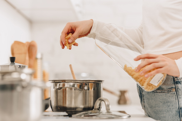 Vue recadrée de fille mettant des pâtes dans la casserole près du poêle de cuisine
 - Photo, image