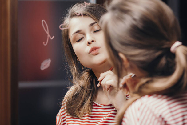 reflection of young woman face in mirror with inscription "I love you", painted heart and lip kiss ,romantic girl send air kiss, concept love and emotions - 写真・画像