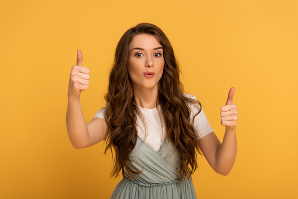 beautiful surprised spring woman showing thumbs up isolated on yellow - Photo, Image