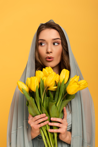zaskoczona kobieta w welonie gospodarstwa bukiet tulipanów izolowanych na żółto  - Zdjęcie, obraz