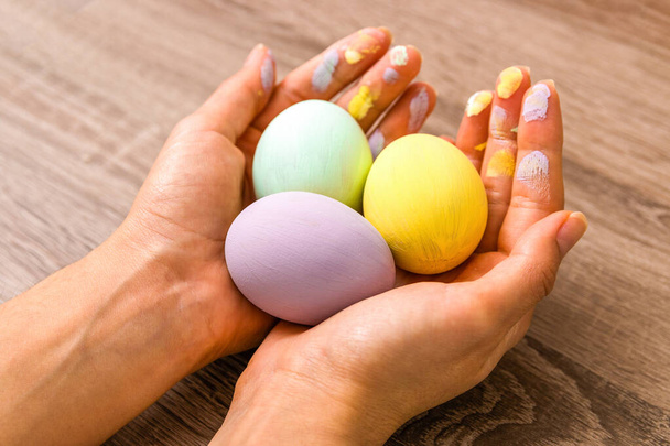 easter concept. closeup beautiful woman hands holding three eggs colored in tender pastel colors yellow, mint and purple over wooden table. - Φωτογραφία, εικόνα