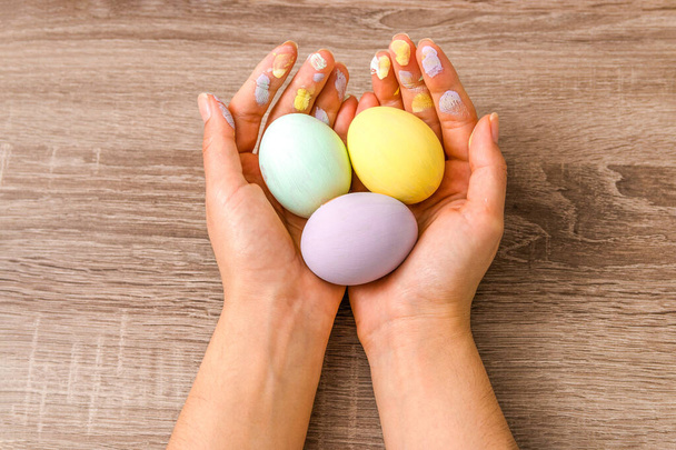 easter concept. closeup beautiful woman hands holding three eggs colored in tender pastel colors yellow, mint and purple over wooden table. - Foto, afbeelding