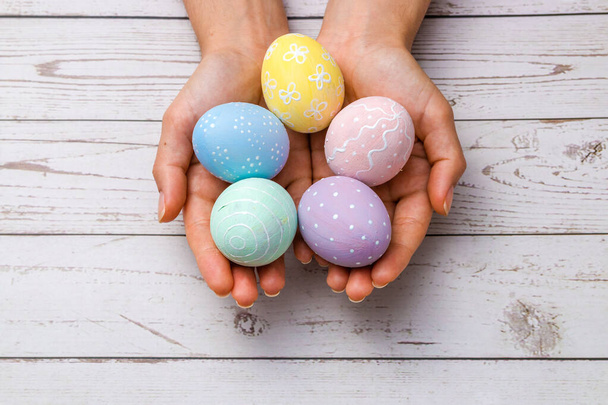 closeup beautiful woman hands holding hand-painted easter eggs in tender pastel colors over wooden table. easter concept. - Photo, Image