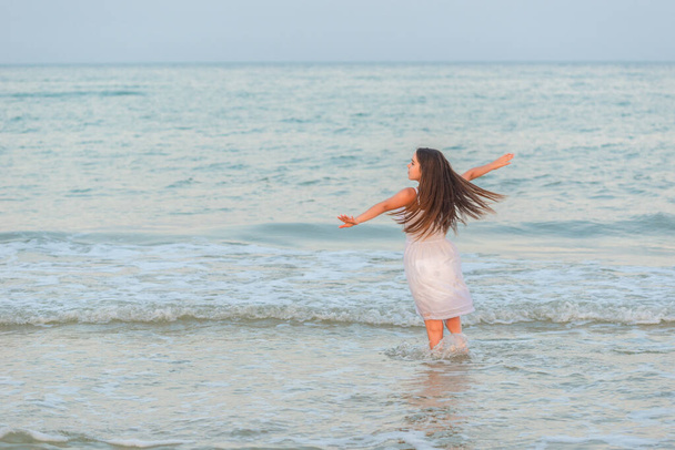 Meisje gelukkig brengt tijd door op het strand en wandelingen langs de zee golven op een zonnige zomeravond tijdens vakantie. - Foto, afbeelding