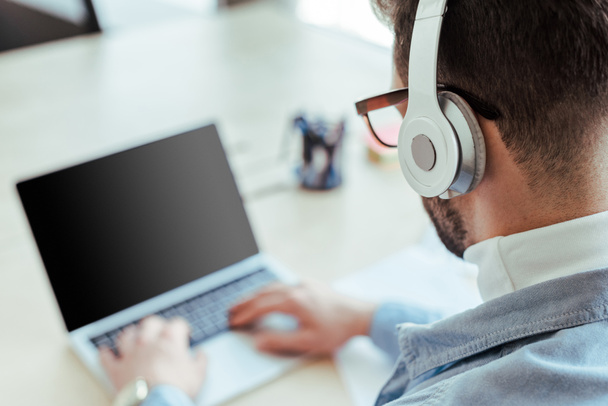 Selective focus of IT worker in headphones working with laptop in coworking space - Foto, Imagen
