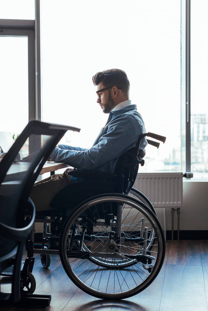 Selektywne ukierunkowanie skoncentrowanego niepełnosprawnego pracownika IT na wózek inwalidzki pracujący w przestrzeni dla współpracowników - Zdjęcie, obraz