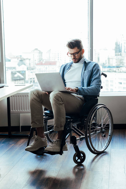 Инвалид ИТ-работник на инвалидной коляске работает с ноутбуком на инвалидной коляске в коворкинге
 - Фото, изображение