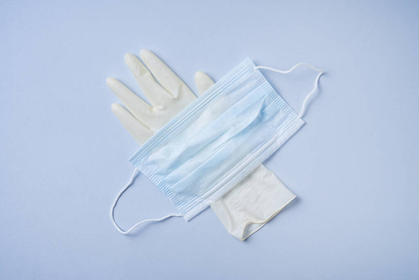 het gezichtsmasker en de medische handschoen hebben een blauwe achtergrond. Coronavirus pandemie, essentiële goederen, schaarste. Bovenaanzicht - Foto, afbeelding
