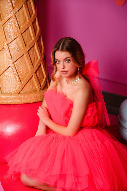 fashion studio photo of beautiful young woman with blond hair in elegant dress posing in pink room with decoration of desserts - Valokuva, kuva