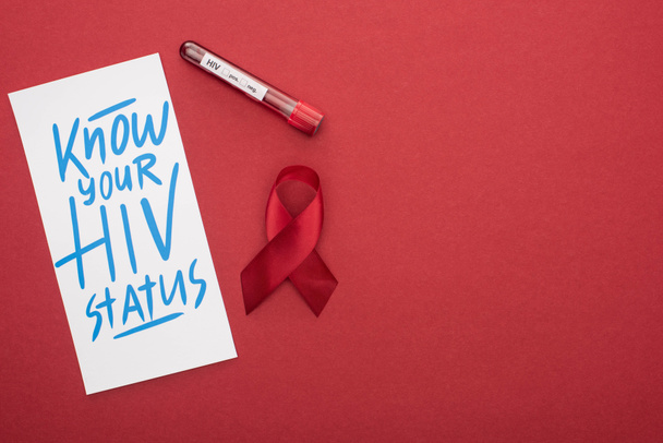 κορυφαία άποψη της κάρτας με γνωρίζουν την κατάσταση του HIV γράμματα και κορδέλα ευαισθητοποίησης με δείγμα αίματος σε κόκκινο φόντο - Φωτογραφία, εικόνα