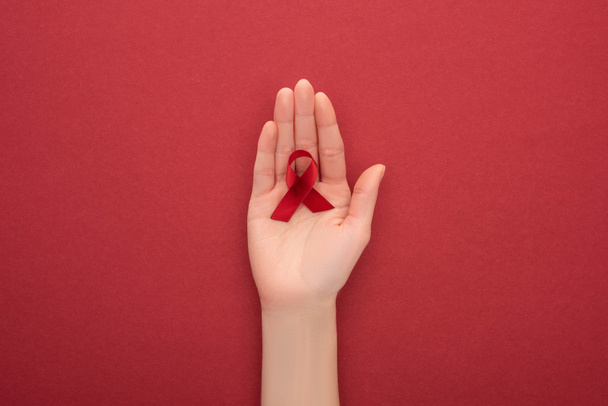 cropped view of woman holding red awareness aids ribbon on red background - Photo, image