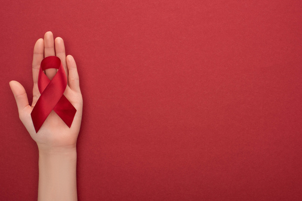 cropped view of woman holding red awareness aids ribbon on red background - Фото, изображение