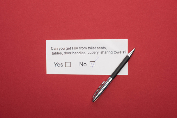 bovenaanzicht van papieren kaart met hiv-vragenlijst en pen op rode achtergrond - Foto, afbeelding