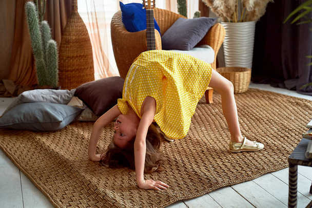 A little charming 6-year-old girl plays sports at home.Flexibility, aerobics, bridge. - Zdjęcie, obraz