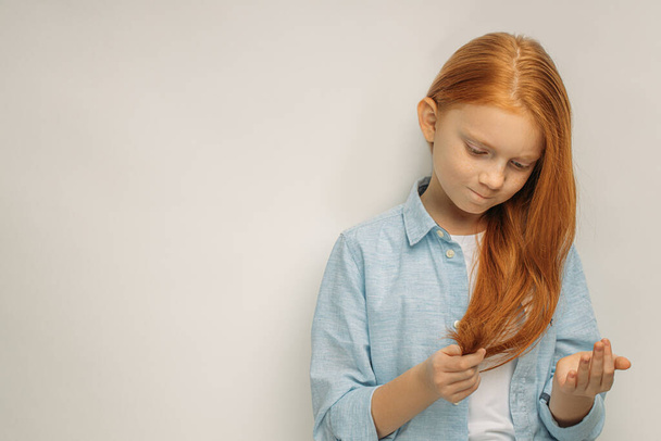 red haired child looks at split ends on hair - Φωτογραφία, εικόνα