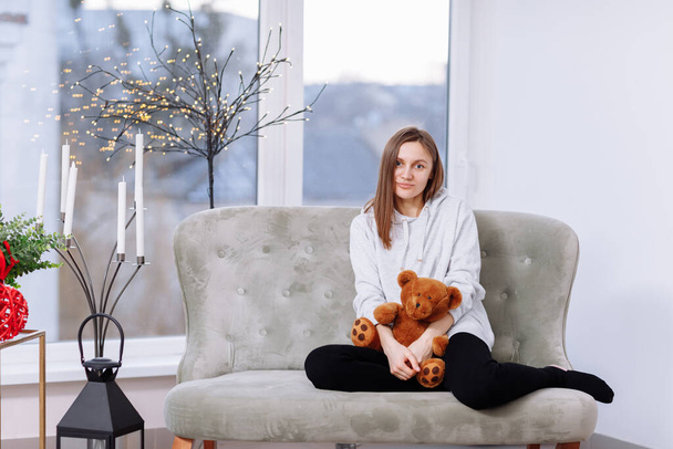 beautiful young smiling woman sitting on the couch hugging teddy bear. - Fotografie, Obrázek