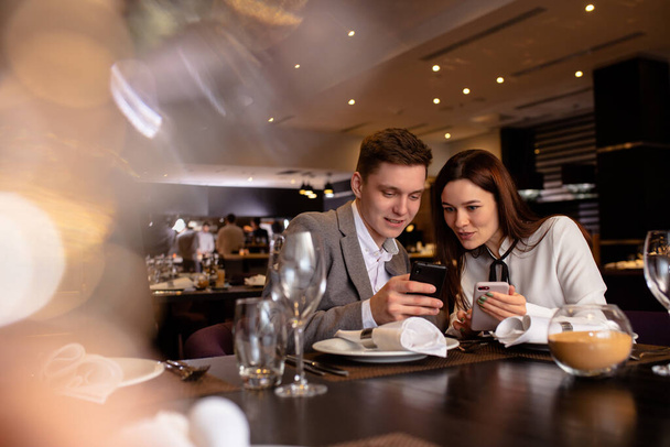 jovem casal caucasiano olhar para smartphone no restaurante
 - Foto, Imagem