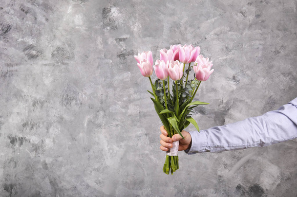 Studio shot of young man wearing cotton shirt, holding beautiful bouquet of pink flowers. Close up, copy space, background. - Foto, afbeelding
