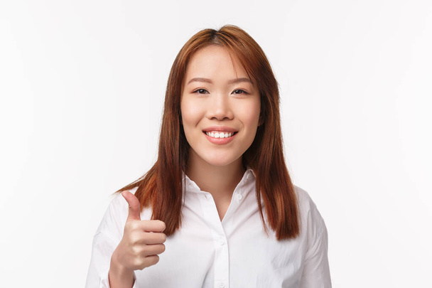 Close-up retrato alegre sorrindo satisfeito mulher asiática em camisa branca, dizer bom trabalho, bom trabalho, fazer gesto de polegar para cima em aprovação ou concordar, aceno aceitavelmente, de pé fundo branco
 - Foto, Imagem