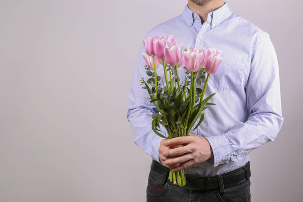 Studio shot of young man wearing cotton shirt, holding beautiful bouquet of pink flowers. Close up, copy space, background. - Foto, Bild