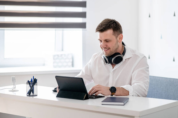 Vue de côté d'un jeune homme cher assis à la maison et travaillant sur un ordinateur portable. Homme caucasien travaillant à partir du bureau à domicile
. - Photo, image