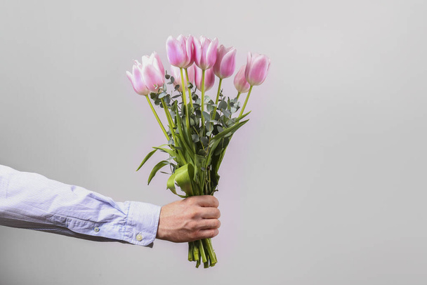 Studio shot of young man wearing cotton shirt, holding beautiful bouquet of pink flowers. Close up, copy space, background. - Fotografie, Obrázek