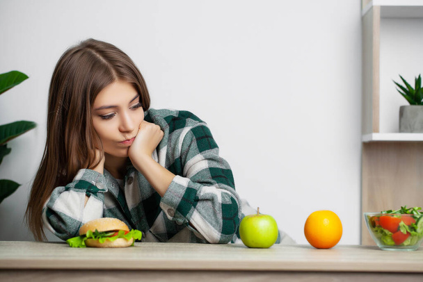 Cute woman makes a choice between healthy and harmful food - Foto, afbeelding