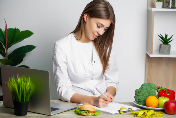 Nainen valkoisessa takissa ravitsemusterapeutti kirjoittaa terveellisen ruokavalion ohjelma laihtuminen
 - Valokuva, kuva