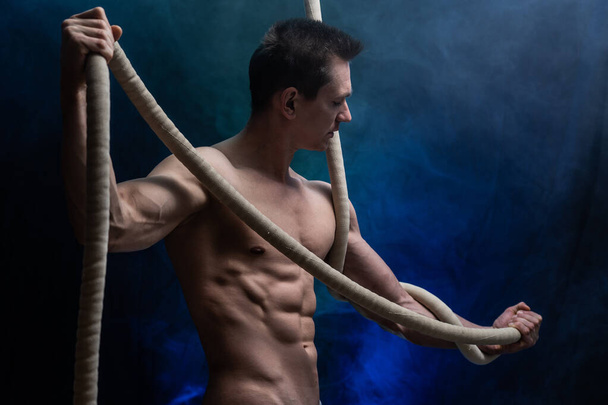 Muscular male circus artist with Cord Lisse on black an smoked background - 写真・画像