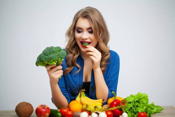 Masada elinde meyve ve sebzelerin arka planında brokoli tutan bir kadın var. - Fotoğraf, Görsel
