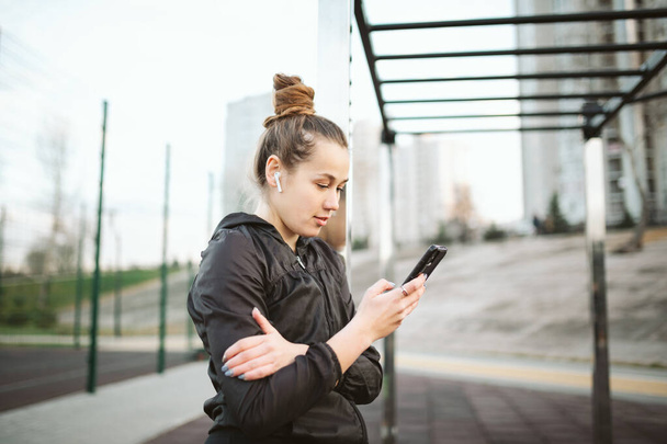 Sportlerin hört Musik per Handy-App für Fitness-Aktivitätstracker Pulsmesser, der Gesundheitsfortschritte auf dem Smartphone verfolgt. Sport und gesund. Kaukasische junge sportliche Frau mit Kopfhörern. - Foto, Bild