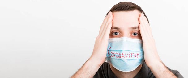 Portrait of young shocked sick man in medical mask with coronavirus word at white background. Respiratory protection. Coronavirus concept.. - Photo, Image