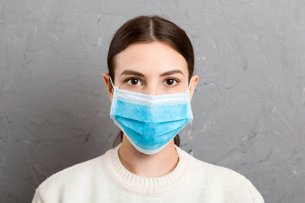 Gri çimento arka planda tıbbi maske takan genç bir kadının portresi. Sağlığınızı koruyun. Coronavirus konsepti. - Fotoğraf, Görsel