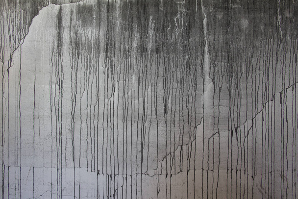 černá barva kapající na šedou stěnu, kapající tekutina, průtok barvy, proud barvy, skvrny, proudové kapky - Fotografie, Obrázek
