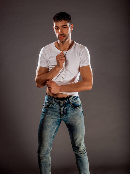 Stylowy facet moda noszenia stylowe niebieskie dżinsy, biały t-shirt podczas pozowania w studio - Zdjęcie, obraz