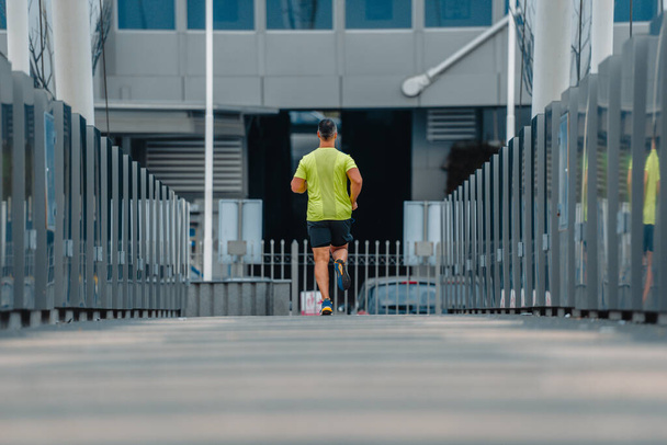 Muskulöser älterer Läufer in Fitnessbekleidung läuft auf einer Brücke - Foto, Bild